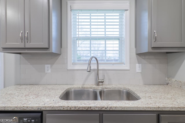 kitchen featuring light stone counters, dishwasher, a sink, and gray cabinetry