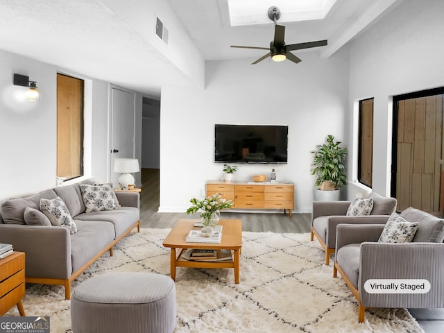 living room featuring a skylight, light wood finished floors, visible vents, ceiling fan, and baseboards