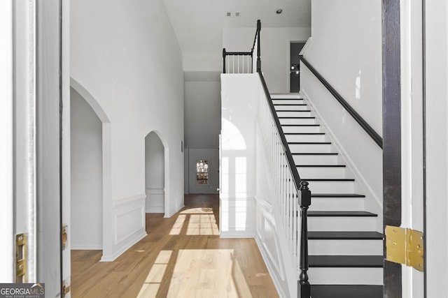 entrance foyer featuring arched walkways, visible vents, a decorative wall, a towering ceiling, and light wood-type flooring