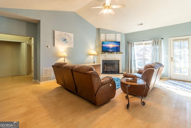 living room with light wood-style floors, vaulted ceiling, visible vents, and a fireplace with raised hearth