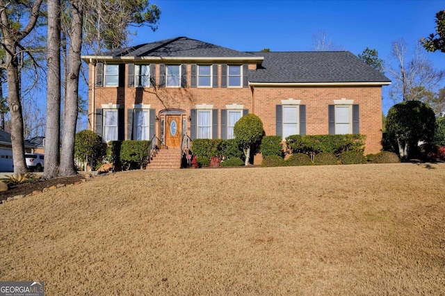 colonial house with brick siding, a front lawn, and a shingled roof