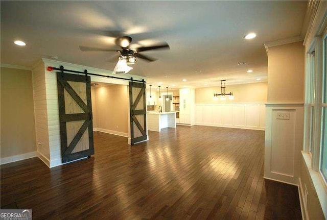 interior space featuring dark wood-type flooring, ornamental molding, ceiling fan, and a barn door