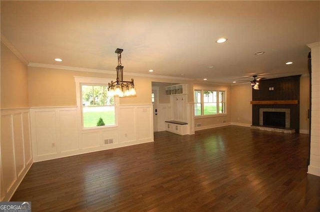 unfurnished living room with ceiling fan with notable chandelier, a fireplace, visible vents, ornamental molding, and dark wood-style floors