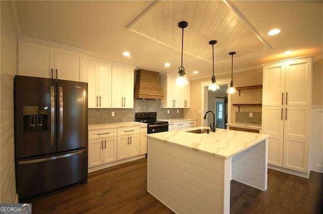 kitchen featuring decorative light fixtures, custom exhaust hood, a kitchen island with sink, light stone countertops, and black appliances