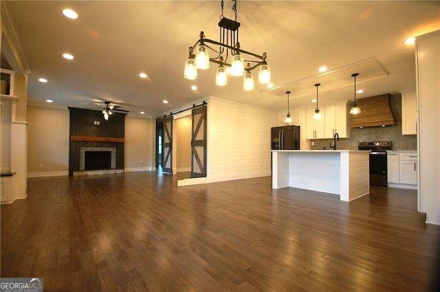 unfurnished living room with ceiling fan, a large fireplace, a barn door, and dark wood-style flooring