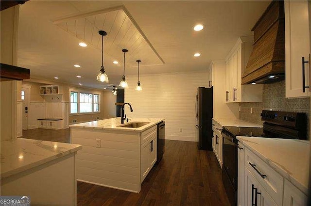 kitchen with white cabinets, decorative light fixtures, a kitchen island with sink, black appliances, and a sink