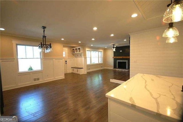 unfurnished living room with ornamental molding, visible vents, a fireplace with raised hearth, and dark wood-style floors