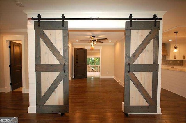 hall with dark wood-style floors, a barn door, baseboards, and crown molding