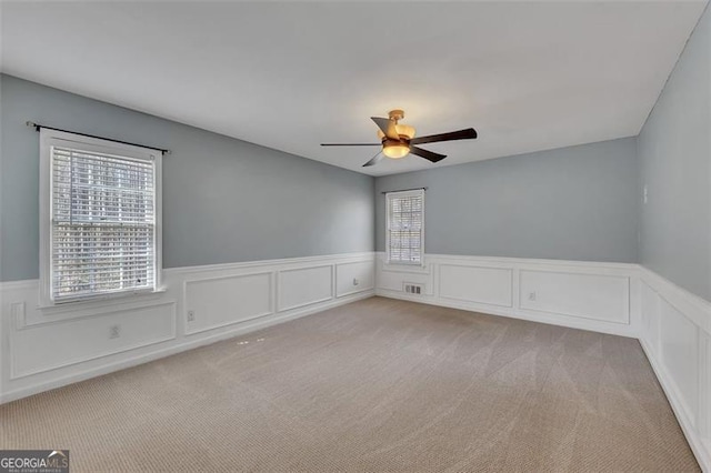 spare room featuring light carpet, ceiling fan, wainscoting, and visible vents