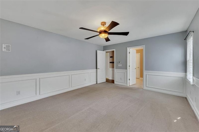 spare room featuring light carpet, a wainscoted wall, and a ceiling fan