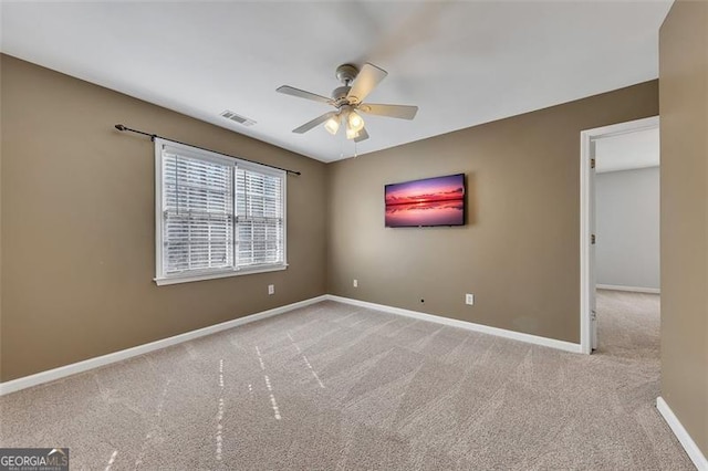 empty room featuring ceiling fan, light colored carpet, visible vents, and baseboards