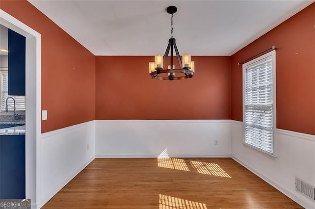 unfurnished dining area featuring visible vents, a sink, an inviting chandelier, and wood finished floors