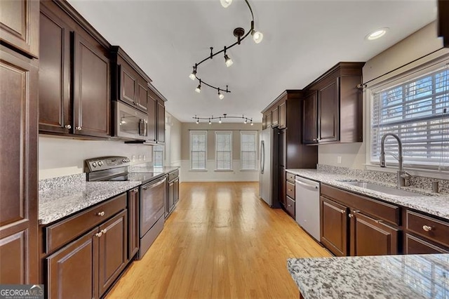 kitchen with stainless steel appliances, a sink, light stone counters, and dark brown cabinets