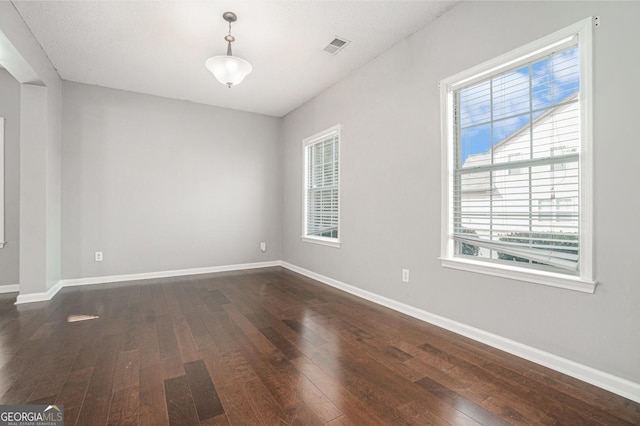 empty room with dark wood-style floors, visible vents, and baseboards