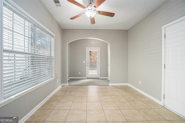 foyer featuring light tile patterned floors, baseboards, visible vents, arched walkways, and a ceiling fan