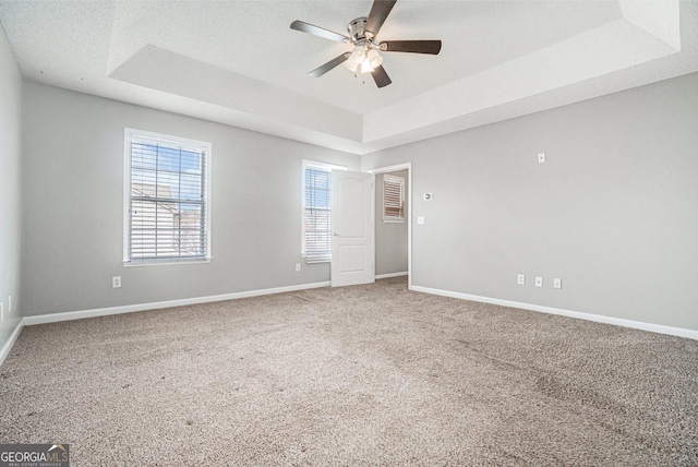 carpeted empty room with ceiling fan, baseboards, a raised ceiling, and a textured ceiling