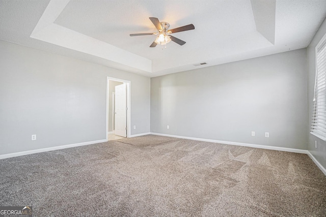 carpeted spare room featuring baseboards, visible vents, a raised ceiling, and a ceiling fan