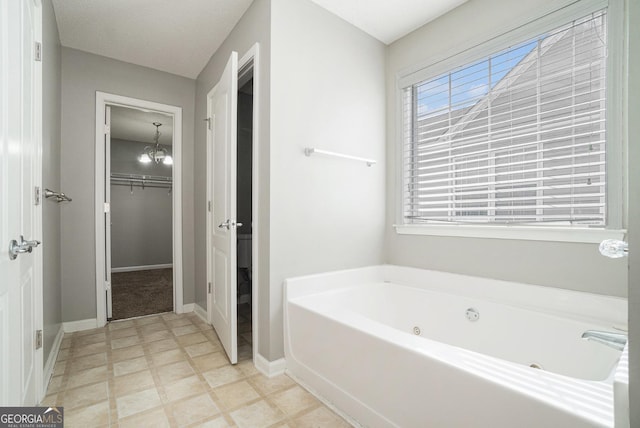 full bathroom featuring a notable chandelier, tile patterned floors, a spacious closet, baseboards, and a tub with jets