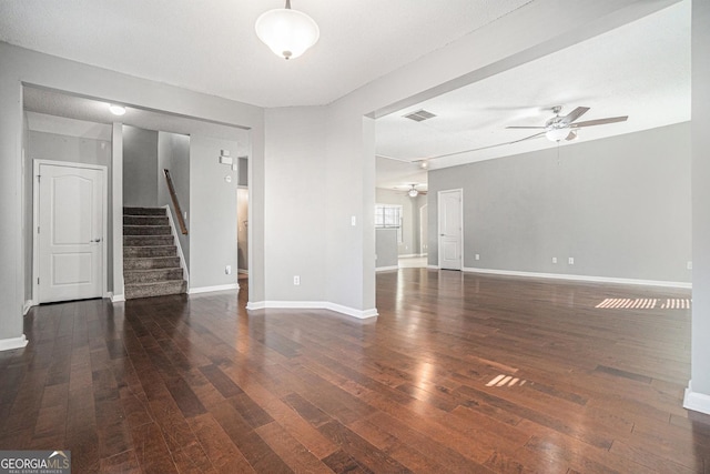 unfurnished living room with wood-type flooring, visible vents, ceiling fan, and stairs