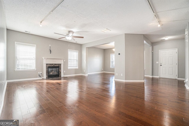 unfurnished living room with a textured ceiling, visible vents, a high end fireplace, a ceiling fan, and dark wood-style floors