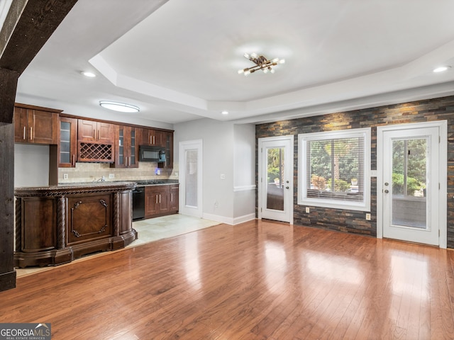 kitchen featuring light wood-style flooring, glass insert cabinets, a tray ceiling, black appliances, and backsplash