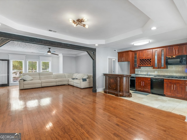 kitchen with visible vents, open floor plan, black appliances, a raised ceiling, and glass insert cabinets