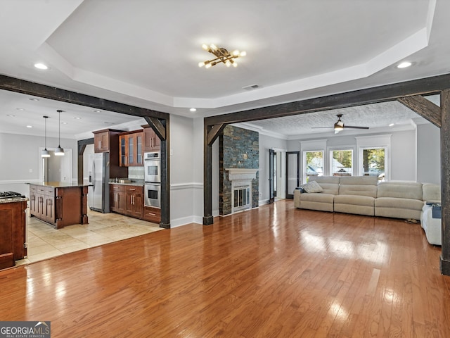 unfurnished living room featuring a fireplace, visible vents, light wood-style floors, a tray ceiling, and crown molding