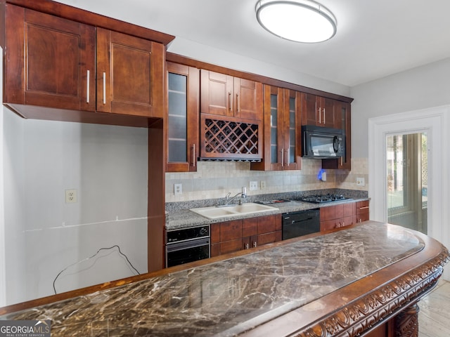 kitchen featuring a sink, decorative backsplash, black appliances, dark stone countertops, and glass insert cabinets