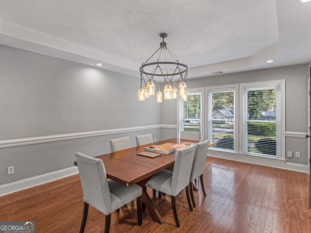 dining area featuring dark wood-type flooring, a raised ceiling, and baseboards