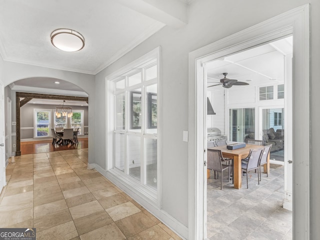 hall with baseboards, arched walkways, beamed ceiling, and ornamental molding