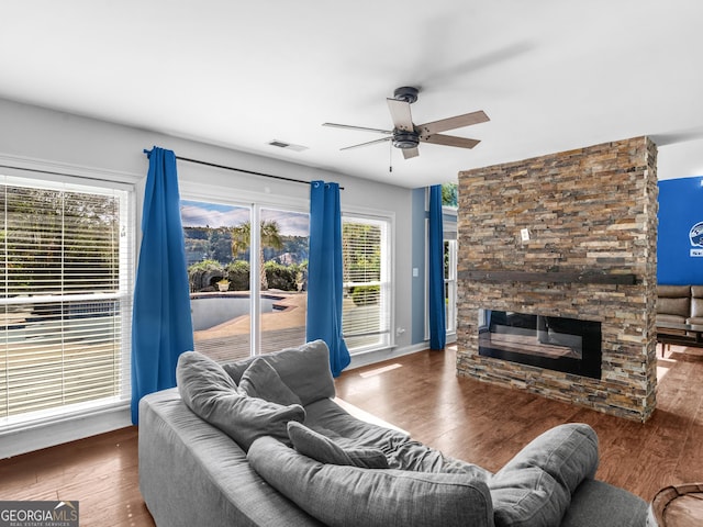 living area with dark wood-type flooring, a fireplace, visible vents, baseboards, and a ceiling fan