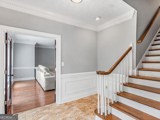 entryway featuring a textured ceiling, stairs, crown molding, and a wainscoted wall