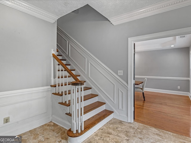 staircase featuring a textured ceiling, ornamental molding, visible vents, and a decorative wall