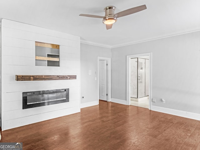 unfurnished living room featuring ornamental molding, a glass covered fireplace, ceiling fan, wood finished floors, and baseboards