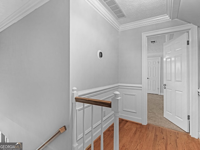 hall featuring a textured ceiling, a decorative wall, an upstairs landing, visible vents, and ornamental molding