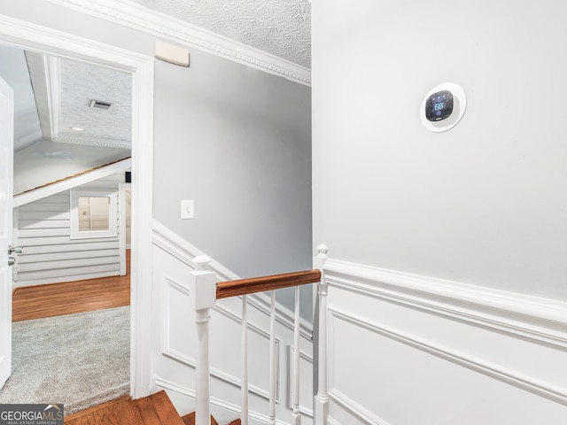 staircase with ornamental molding, a wainscoted wall, visible vents, and a textured ceiling