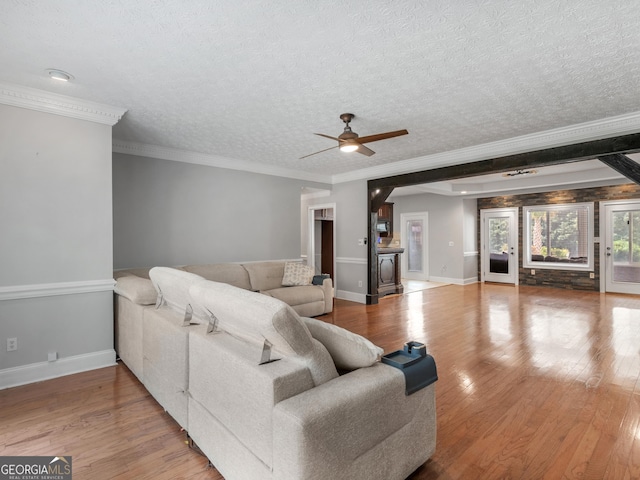 living area with a textured ceiling, wood finished floors, a ceiling fan, baseboards, and ornamental molding