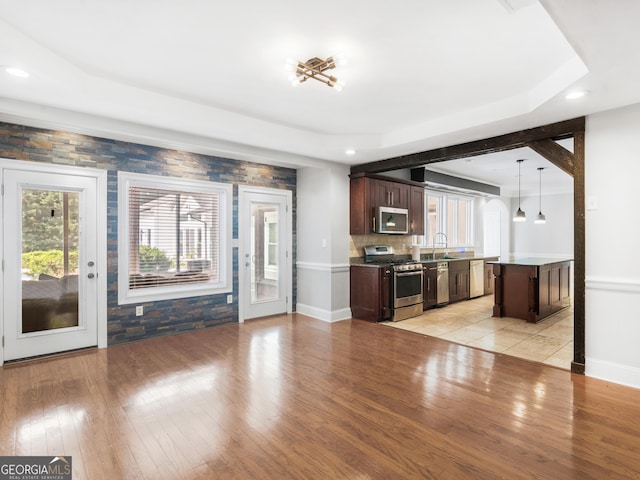 kitchen featuring dark brown cabinetry, a kitchen island, hanging light fixtures, stainless steel appliances, and a sink