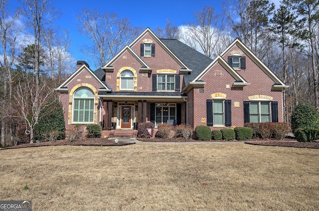 view of front of property with covered porch, brick siding, a front lawn, and a chimney