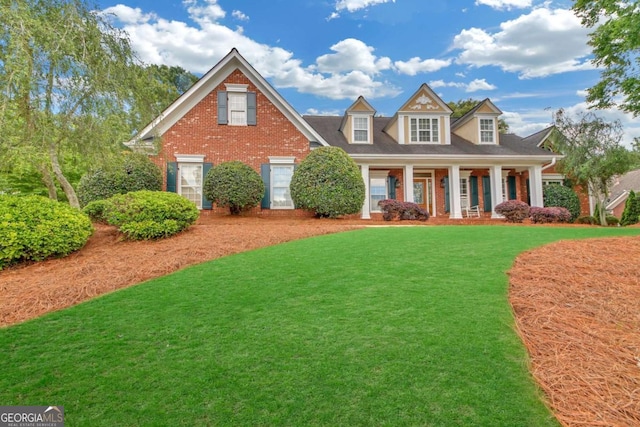 cape cod-style house featuring a front yard, covered porch, and brick siding