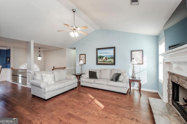 living area featuring lofted ceiling, visible vents, a stone fireplace, and wood finished floors