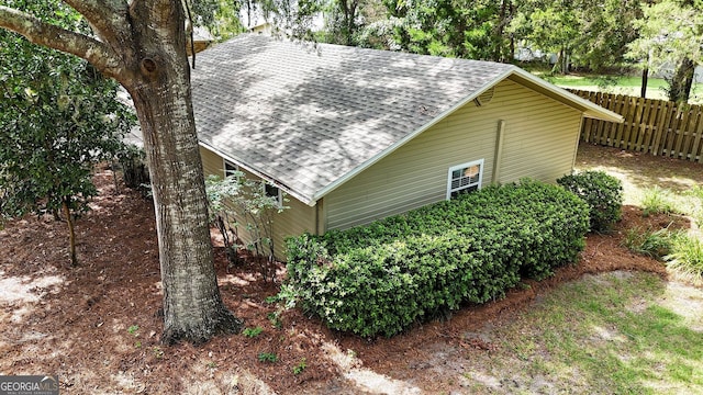 view of home's exterior featuring roof with shingles and fence