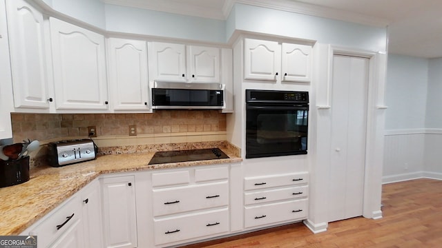 kitchen featuring crown molding, light wood finished floors, white cabinets, light stone countertops, and black appliances