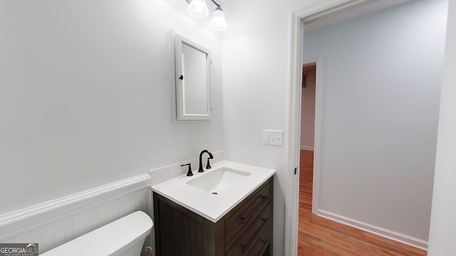 half bathroom with toilet, wainscoting, wood finished floors, and vanity