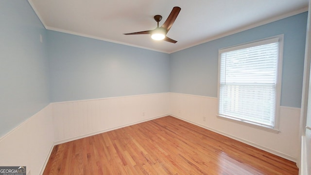 unfurnished room with light wood finished floors, a ceiling fan, ornamental molding, and a wainscoted wall