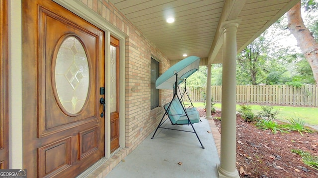 view of exterior entry with covered porch, fence, and brick siding