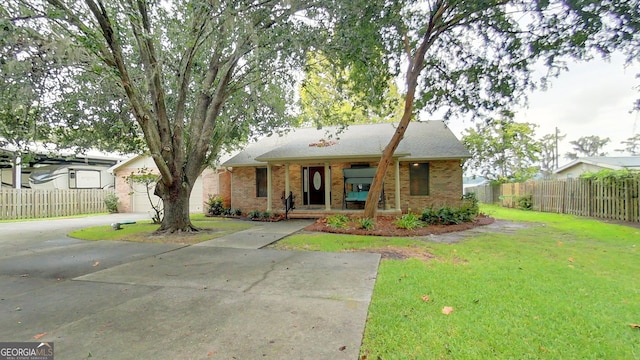 view of front of home with driveway, brick siding, a front yard, and fence