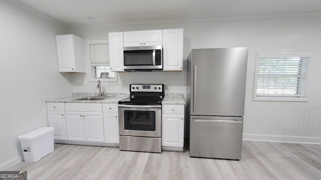 kitchen with light wood-style flooring, a sink, white cabinets, ornamental molding, and appliances with stainless steel finishes