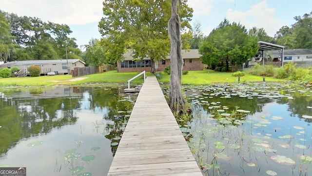 view of dock featuring a lawn, a water view, and fence