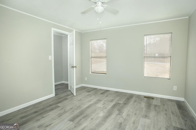 spare room with visible vents, a ceiling fan, baseboards, ornamental molding, and light wood finished floors